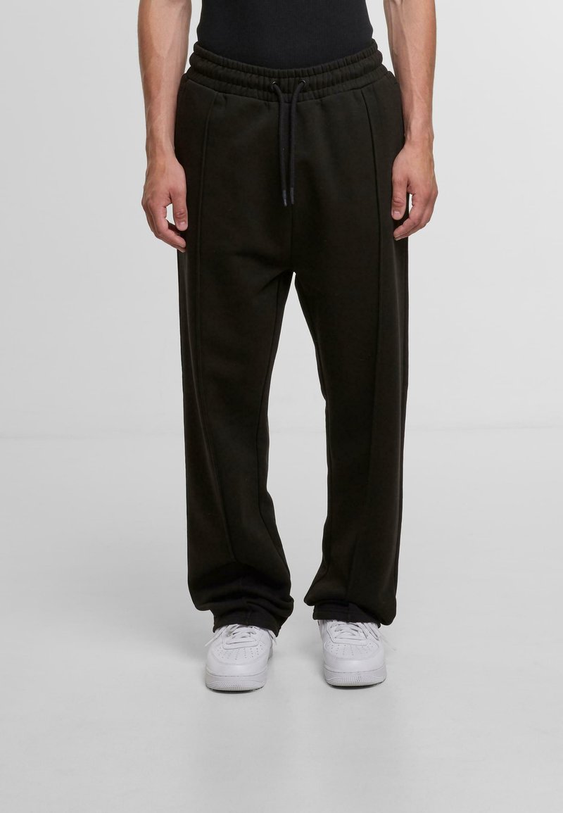 Black sweatpants with an elastic waistband and drawstring, featuring side seams and a relaxed fit, paired with white sneakers.