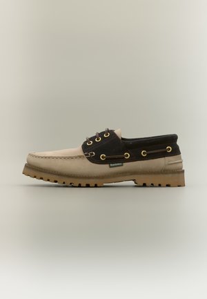 Beige and dark brown lace-up boat shoe with a textured upper, gold eyelets, and a rugged rubber sole featuring deep treads.