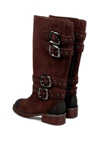 Botas de ante marrón hasta la rodilla con acentos negros, que presentan tres correas y hebillas cuadradas, además de una puntera redondeada con un tacón apilado.