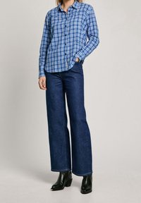 Blue plaid button-up shirt paired with dark blue wide-leg jeans and black ankle boots, showcasing a casual, layered look.