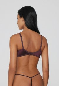 Burgundy bra with adjustable straps, smooth texture, and hook closure, paired with matching thong, showcasing minimalistic design and form-fitting shape.