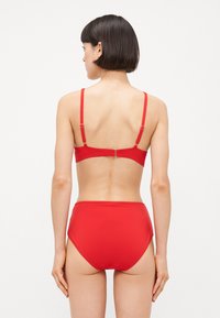 Rdeča bikini komplet z vrhnjim delom v tarzdu halter s nastavljivimi trakovi in visokim pasom. Gladek, raztegljiv material z minimalnimi podrobnostmi.