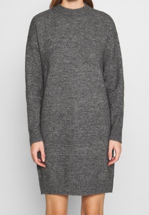 Kvinde iført en langærmet, knælængde, mørkegrå strikket sweaterkjole mod en ensfarvet baggrund.