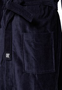 Marineblaue Corduroy-Bademantel mit Taillenknoten, aufgesetzten Taschen und einem CR7-Logoschild, das den strukturierten Stoff und das durchdachte Design hervorhebt.