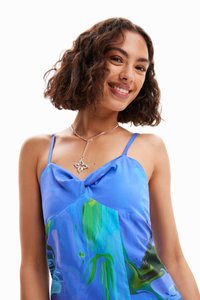 Rochie fără mâneci de culoare albastră, cu un model abstract ce include accente verzi, design cu nod în față și o textură satinată. Detalii din bijuterii argintii.