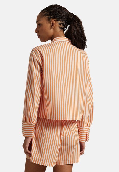 Pomarańczowo-biała kurtka w paski z długimi rękawami, o krótkim kroju. W komplecie dopasowane szorty w paski, ukazujące gładką fakturę tkaniny.