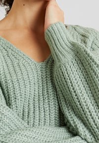 Ljusgrön stickad tröja med V-ringning, med kraftig ribbad textur och breda ärmar. Mjukt material med en mysig framtoning.