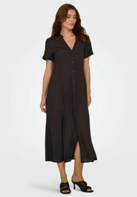Robe midi noire à boutons, à manches courtes, décolleté en V et fente sur le devant, réalisée dans un tissu lisse et léger. Design simple et minimaliste.