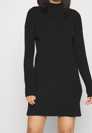 Schwarzes geripptes Strickkleid mit hohem Kragen, langen Ärmeln und taillierter Silhouette, das eine vertikale Textur aufweist und in mittlerer Oberschenkelhöhe endet.
