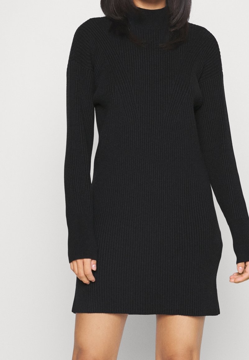 Abito a maglia nero a coste con collo alto, maniche lunghe e silhouette aderente, caratterizzato da una texture verticale e lunghezza fino a metà coscia.