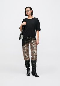 Černé předimenzované tričko s krajkovým lemováním, leopardí potisk joggerů a černé kožené kozačky sahající po kolena; doplňky zahrnují černou kabelku a brýle.