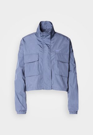 Jachetă scurtă, de culoare albastru deschis, realizată dintr-un material neted, cu guler înalt, două buzunare frontale și manșete elastice.