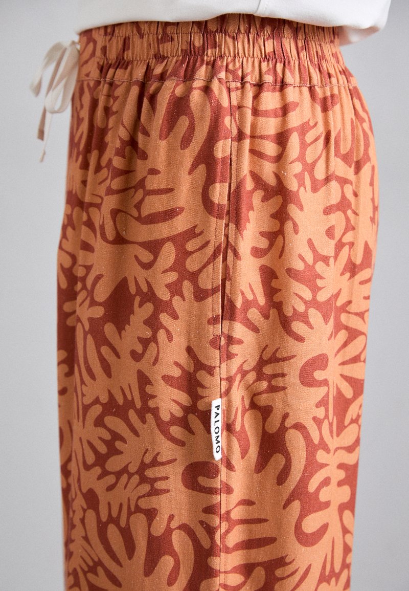 Orange patterned pants with an elastic waistband and decorative drawstring. The fabric features a bold abstract design in darker orange.