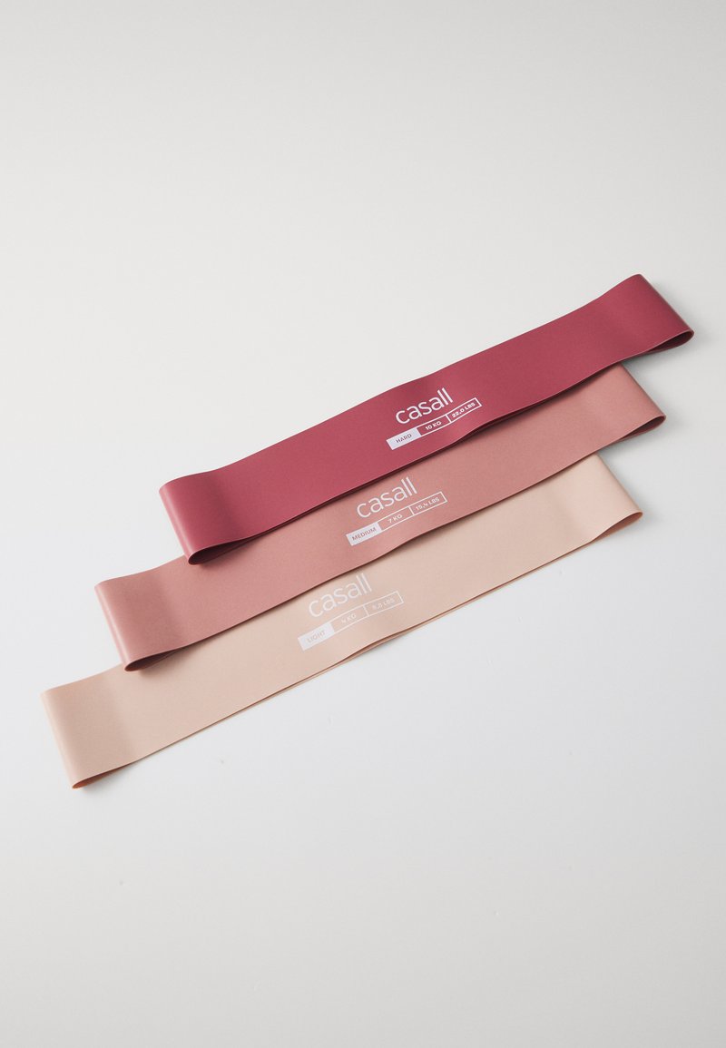 Three resistance bands in varying shades: dark red, soft pink, and light nude. Each band features a white label with brand and strength indicators.