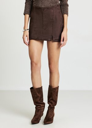 Brauner Minirock aus Wildleder mit einem vorderen Schlitz und glatter Textur. Kombiniert mit kniehohen braunen, lässigen Stiefeln.