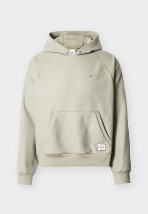 Svetlo bež pulover iz flisa s kapuco, sprednjim žepom, majhnim Nike logotipom na prsih in pravokotno belo tkanino etiketo ob pasu.