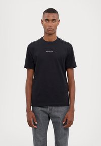 T-shirt en coton noir avec un col rond, des manches courtes et un logo "MICHAEL KORS" blanc sur la poitrine. Texture lisse et coupe classique.