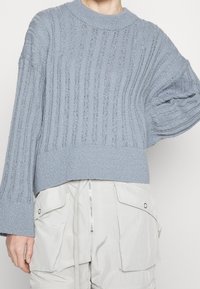 Maglione lavorato a maglia light blue con righe verticali, maniche larghe e orlo corto, realizzato in un morbido materiale testurizzato.