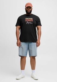 Juodas marškinėlis su ryškiomis spalvomis "JACK & JONES" logotipu; derinamas su šviesiai mėlynomis džinsinėmis šortais ir baltais sportbačiais. Papildyta smėlio spalvos kepure.