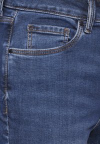 Jeans de mezclilla con un lavado azul oscuro y desgaste visible. Costuras en contraste en los bolsillos y las costuras con un diseño clásico de cinco bolsillos.