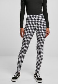 Leggings en pied-de-poule noir et blanc avec une taille haute, associées à un haut noir à manches longues et des baskets noires avec des semelles blanches.