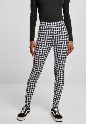 Black and white houndstooth leggings with a high waistband, paired with a long-sleeve black top and black sneakers with white soles.