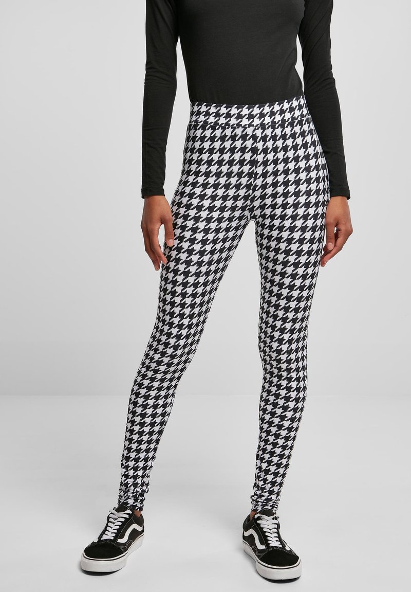Zwart-witte houndstooth legging met een hoge tailleband, gecombineerd met een zwart longsleeve en zwarte sneakers met witte zolen.