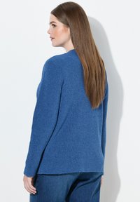Blauer Strickpullover mit langen Ärmeln, einem runden Ausschnitt und einem am Rücken etwas längeren Saum. Weicher Stoff und gerippte Details überall.