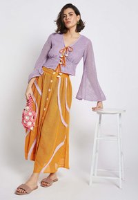 Lavender knit cropped top with bell sleeves and orange drawstring, paired with a long orange skirt featuring pink wavy stripes and button accents.