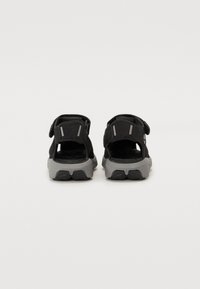 Sandalias negras con correas ajustables, diseño transpirable y una suela de goma gris con detalles texturizados en la parte inferior para mayor tracción.