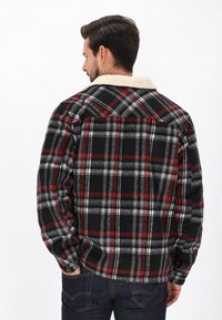 Fekete, piros és szürke kockás flanel ing, krém színű műszőrme gallérral. Gombos kialakítás, hosszú ujjak és laza szabás.