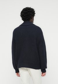 Tamno mornarsko plava pletena pulover s ležernim krojem, rebrastim rubom i dugim rukavima; sadrži ovratnik i strukturiranu tkaninu.