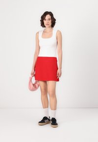 Top alb, fustă scurtă roșie, adidași negri cu accente albe și geantă roz. Materiale netede cu un design ajustat. Aspect curat și modern.