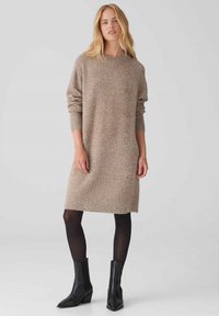 Abito di maglina in un mix di beige e argento, con scollatura rotonda, maniche lunghe e vestibilità morbida; abbinato a stivali neri alla caviglia.