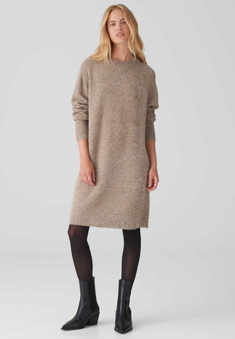 Abito di maglina in un mix di beige e argento, con scollatura rotonda, maniche lunghe e vestibilità morbida; abbinato a stivali neri alla caviglia.