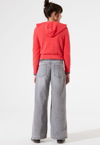 Sudadera recortada y borrosa en un brillante color coral, con capucha y dobladillo de rayas en blanco y negro, combinada con jeans de mezclilla de pierna ancha en un tono gris claro que cuentan con bolsillos.