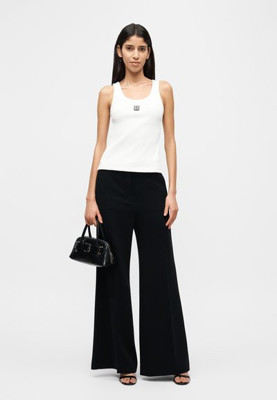 Λευκό ριμπ αμάνικο τοπ με μικρό λογότυπο, σε συνδυασμό με μαύρο παντελόνι φαρδιάς γραμμής. Αξεσουάρ περιλαμβάνουν μαύρη τσάντα χειρός και σανδάλια ανοιχτής μύτης.