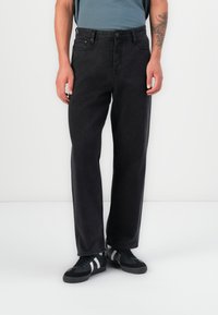 Jeans negri din denim cu croială dreaptă, cinci buzunare, închidere cu nasture și detalii de cusătură discrete. Purtați cu pantofi sport negri.