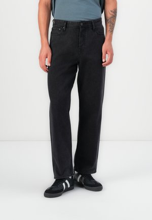 Black denim straight-leg jeans with five pockets, a button closure, and subtle stitching details. Worn with black athletic shoes.
