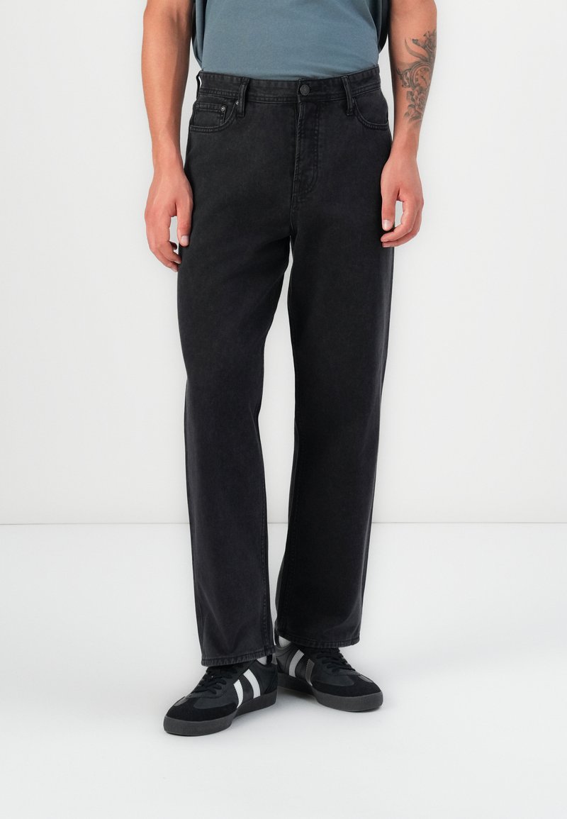 Jeans negri din denim cu croială dreaptă, cinci buzunare, închidere cu nasture și detalii de cusătură discrete. Purtați cu pantofi sport negri.