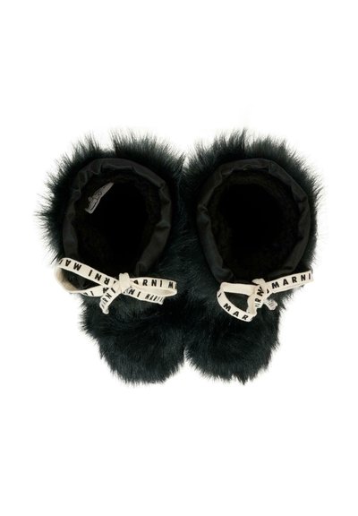 Chaussons en fourrure noire avec un intérieur doux, présentant une bordure en tissu noir et un détail en ruban blanc avec logo à l'ouverture.