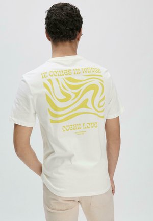 Witte katoenen t-shirt met een gele golvende print op de achterkant met de tekst "HET KOMT IN Golven" en "OCEAN LIEFDE" daaronder. Korte mouwen, ronde hals.