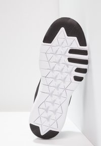 Suola di scarpa atletica in bianco e nero con motivo a presa testurizzato, tacche triangolari e un design geometrico distintivo.