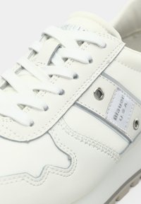 Baskets en cuir blanc avec une bande grise accentuée, des œillets ronds en métal et une semelle texturée. Dotées de lacets en tissu et d'un logo sur le côté.