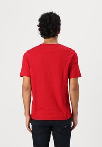 T-shirt rouge à manches courtes en coton doux avec un col rond classique et un ourlet droit, porté avec un jean foncé. Aucun motif ou logo visible.