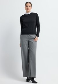 Zwarte lange mouwen top met een gerimpelde witte kraag, gecombineerd met grijze wijde broek. Zwarte hoge hakken maken de outfit compleet.