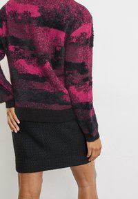 Suéter difuso con rayas horizontales en rosa y negro; combinado con una falda negra texturizada. El suéter tiene mangas largas y un corte relajado.