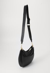 Bolso de hombro de cuero negro con forma curva, que presenta herrajes dorados y una correa texturizada grabada con el nombre de la marca.