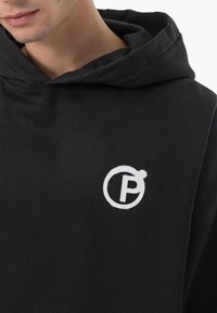 Schwarzer Kapuzenpulli aus Baumwolle mit verstellbarem Kapuzenzug. Auf der Brust befindet sich ein weißes, rundes Logo mit dem Buchstaben "P". Weicher Stoff.