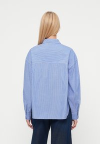 Μπλε και λευκό ριγέ πουκάμισο με κουμπιά, άνετη γραμμή, μακριά μανίκια και σχέδιο πίσω καβάλου. Βαμβακερό ύφασμα, λεπτομέρεια με τσέπη στο μπροστινό μέρος.